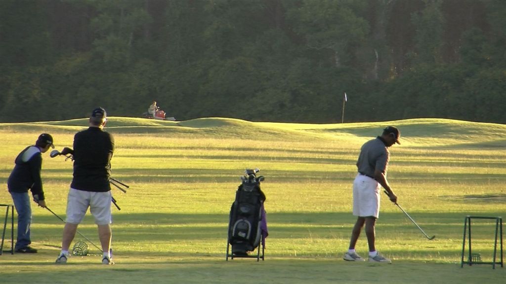 A group of men practice on the driving range at Country Oaks Golf Course