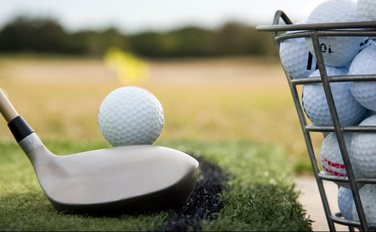 golf club by golf ball next to bucket of golf balls